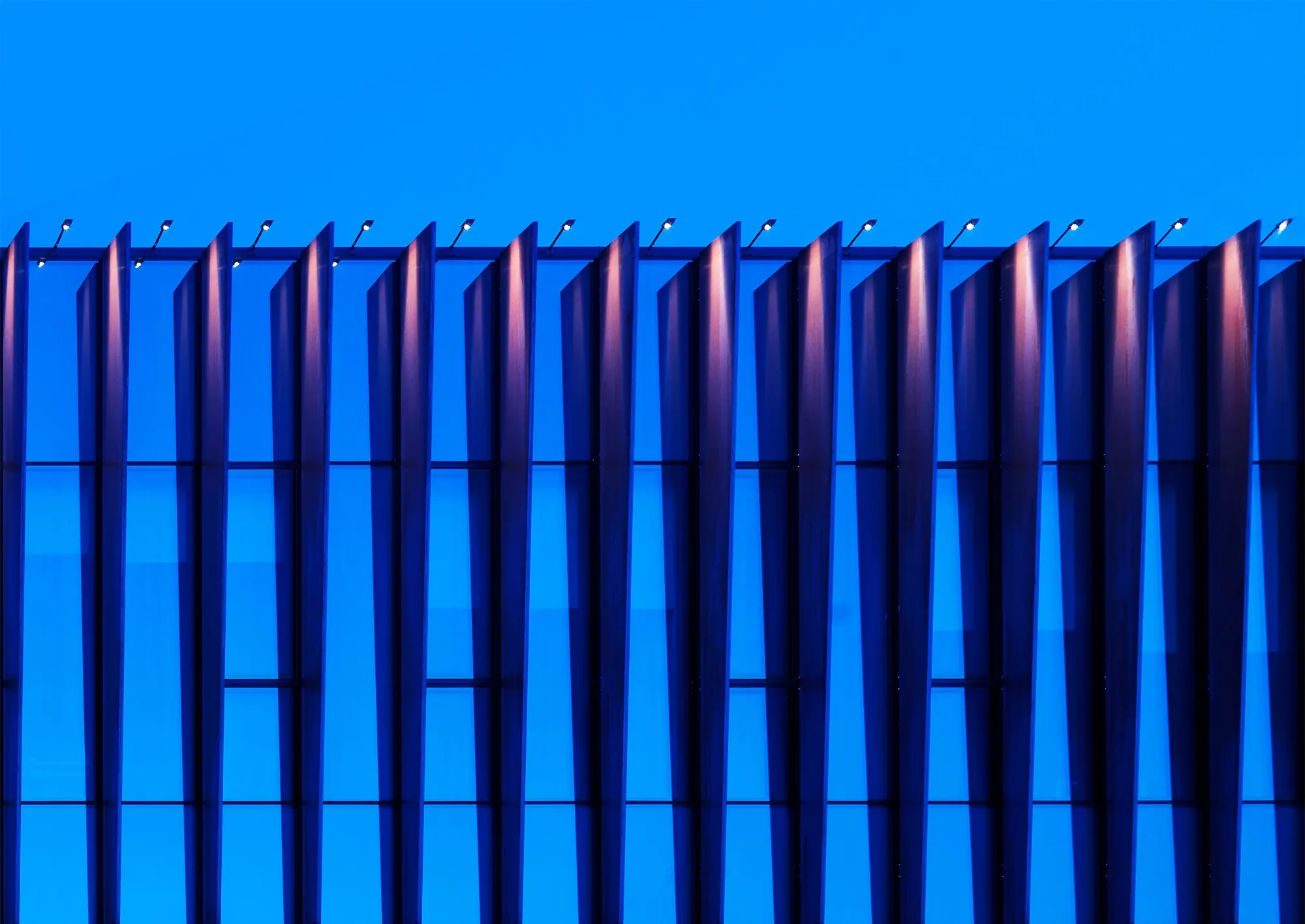 Close view of copper fins against a deep blue dusk sky, each lit by a narrow grazing beam