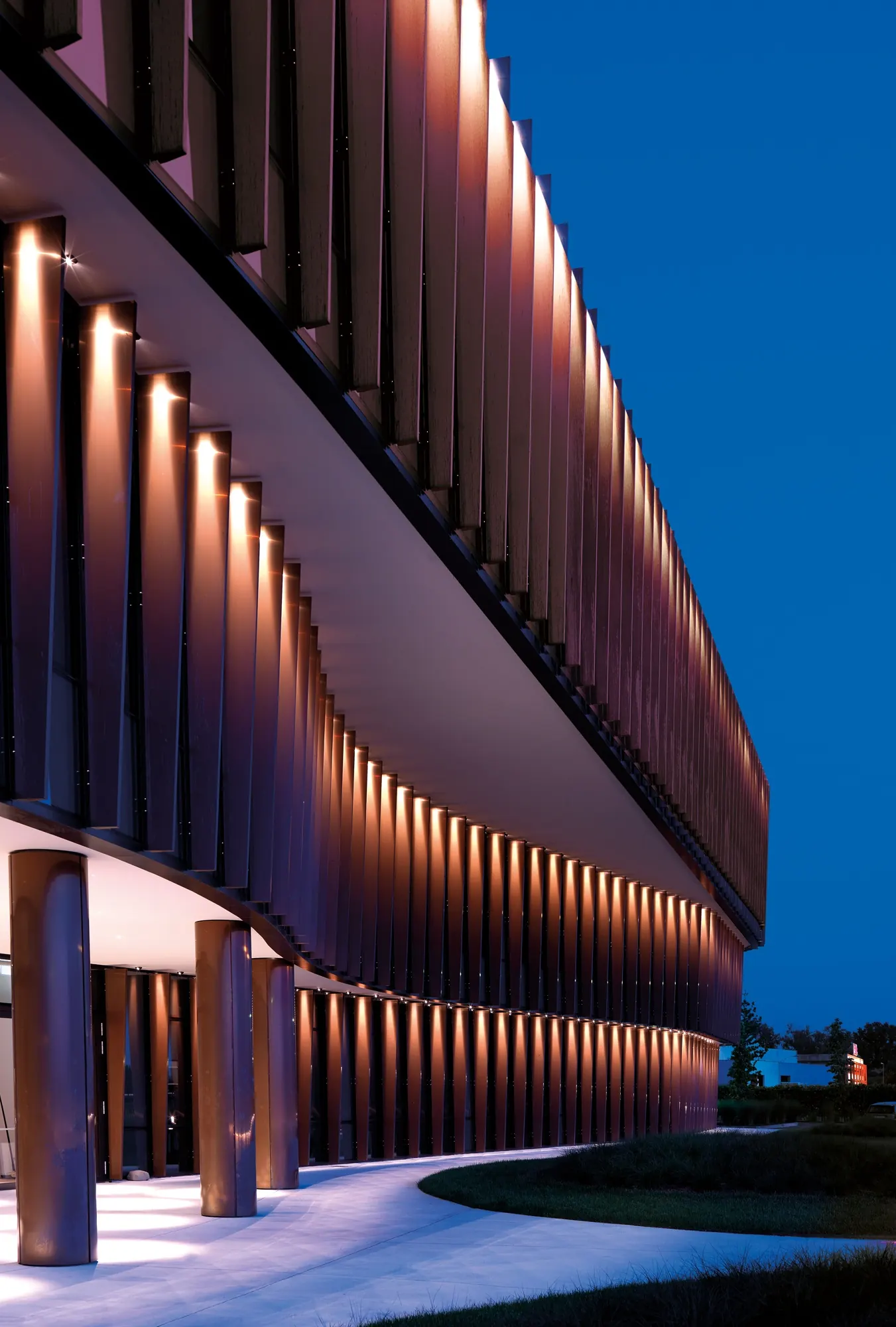 Tall run of fins lit from below beside an entrance canopy, ground lights in the lawn
