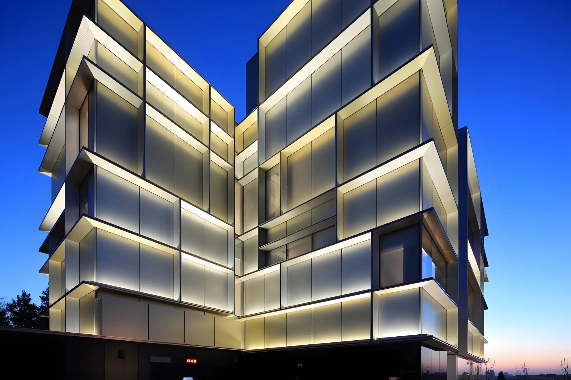 A stepped glass facade outlined in warm linear light at dusk, every frame edge glowing